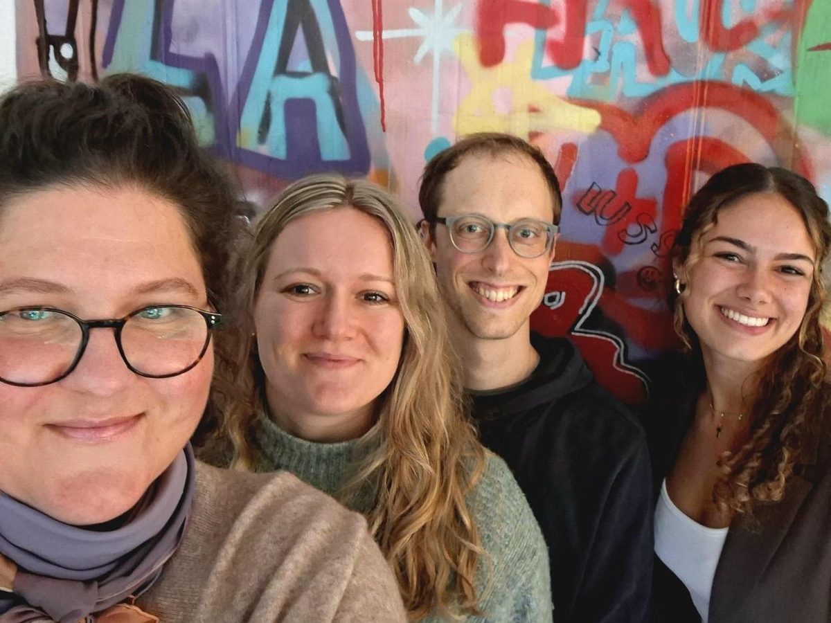 Das Team Feuervogel: vier Menschen lächeln vor einer bunten Graffiti-Wand in die Kamera
